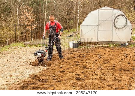 Spring Preparation Soil For Seeding With Tiller. Spring Work In The Garden. Farmer Plows The Land Wi