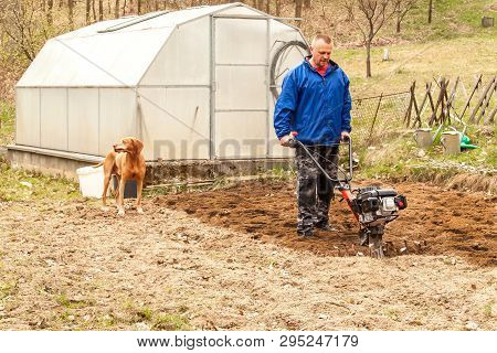 Spring Preparation Soil For Seeding With Tiller. Spring Work In The Garden. Farmer Plows The Land Wi