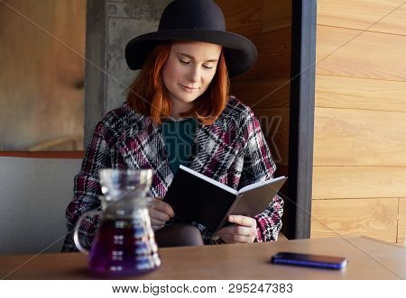 Closeup Portrait Of Young Attractive European Redheaded Freckled Woman In Hat And Coat, Sitting In T