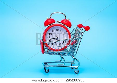 Red Retro Alarm Clock In Shopping Cart On Blue Background. Shopping Time, Market, Consumer Concept.