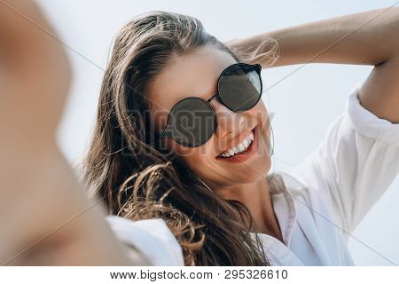 Close-up Of Young Beautiful Woman In Sunglasses Smiling Holding Camera And Smiling While Taking Self