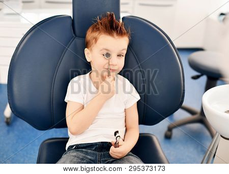 Kid Boy In Modern Dental Chair Plays A Dental Mirror And Smiles In Stomatologist Office