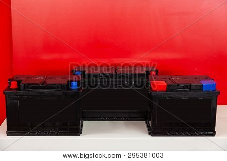 Three New Black Rechargeable Batteries For Car And Vehicle Stand  On A Red Background With White Ins