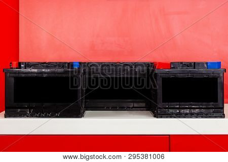 Three New Black Rechargeable Batteries For Car And Vehicle Stand  On A Red Background With White Ins