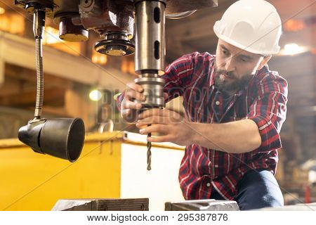 Young engineer or machinebuilder checking large industrial drill before using it in processing work