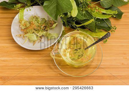 Linden Flower Tea In The Glass Cup With Spoon And Dried Linden Flowers On Saucer On Wooden Surface A