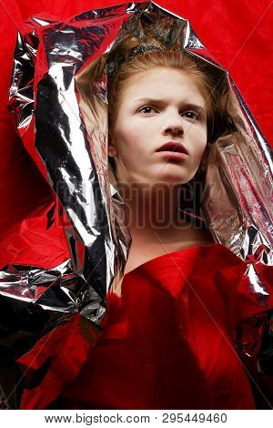 Arty Portrait Of A Fashionable Red-haired Model In Red With Silver Foil Cape Over Red Curtain Backgr