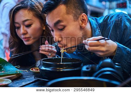 Young Chainese Couple Trying Asian Food At First Time. Couple Is Siting At Cafe Outside. They Have C