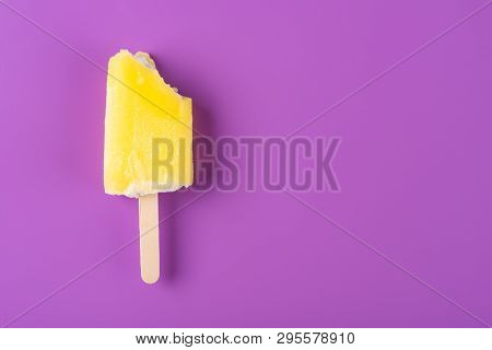 Yellow Popsicle With Some Bites On A Purple Background