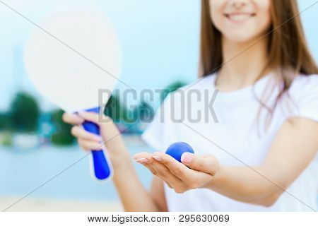 Young Smiling Woman In Light Clothes Is Holding White Racket And Ball In Her Hands. Cheerful Female 