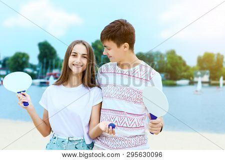 Young Smiling Woman In Light Clothes Is Holding White Racket And Ball In Her Hands. Cheerful Female 