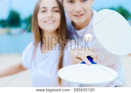 Young Smiling Woman In Light Clothes Is Holding White Racket And Ball In Her Hands. Cheerful Female 