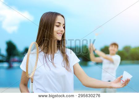 Young Smiling Woman In Light Clothes Is Holding White Racket And Ball In Her Hands. Cheerful Female 