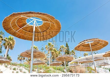 Reed Beach Umbrellas, Sunshades Against Blue Sky On The Beach. Bamboo Parasols, Straw Umbrellas On O