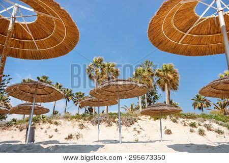 Reed Beach Umbrellas, Sunshades Against Blue Sky On The Beach. Bamboo Parasols, Straw Umbrellas On O