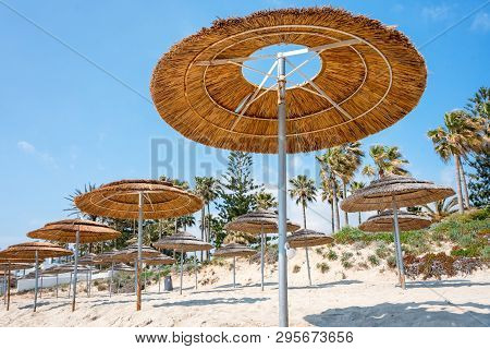 Reed Beach Umbrellas, Sunshades Against Blue Sky On The Beach. Bamboo Parasols, Straw Umbrellas On O