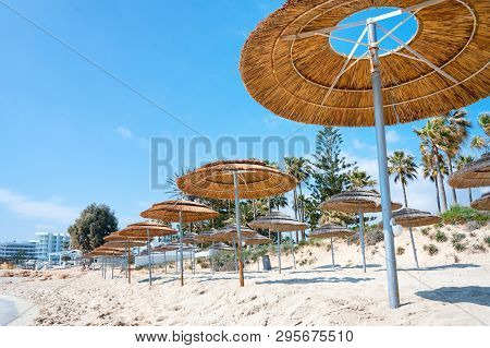 Reed Beach Umbrellas, Sunshades Against Blue Sky On The Beach. Bamboo Parasols, Straw Umbrellas On O