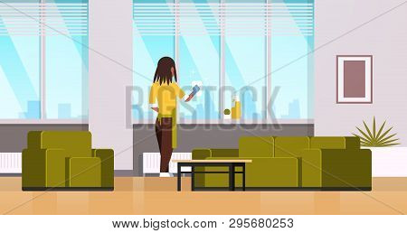Woman In Gloves And Apron Cleaning Windows With Rag Cleaner Spray Rear View African American Housewi