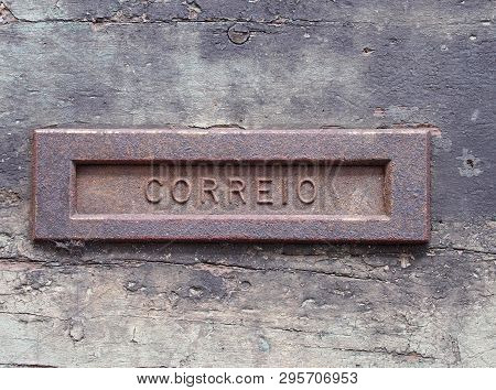 An Old Rusting Iron Letterbox In A Black Wooden Door With Chipped Peeling Paint With The Word Correi