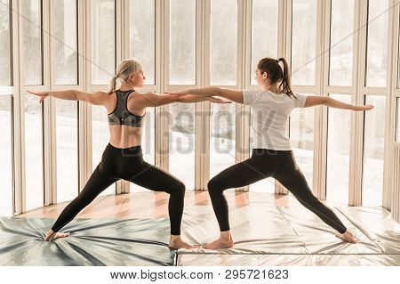 Two Beautiful Girls Practicing Yoga. Warrior Pose - Virabhadrasana. Yoga Concept, Healthy Lifestyle