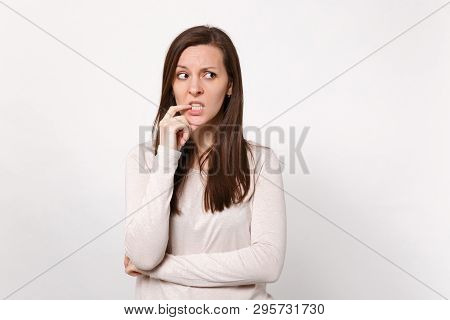 Portrait Of Preoccupied Pensive Young Woman In Light Clothes Looking Aside, Gnawing Nails Isolated O