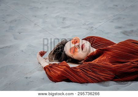 Style Adult Woman In Sunglasses And Burgundy Color Blouse Lying Down On On A Sand, Beach. Above Ivew