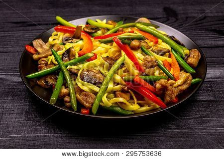 Appetizing Stir Fried Noodles With Garlic Sprouts, Mushrooms, Red Pepper And Chicken Meat On A Black