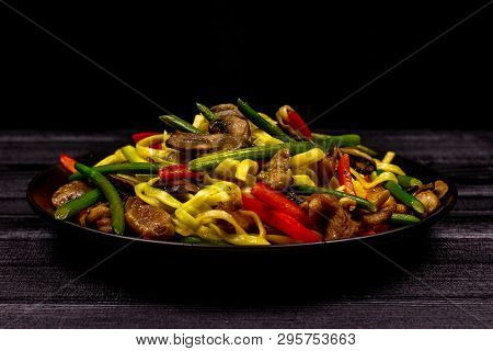 Appetizing Stir Fried Noodles With Garlic Sprouts, Mushrooms, Red Pepper And Chicken Meat On A Black