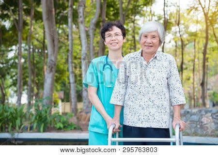 Disabled Senior Asian Woman Walking With Assistance From Nurse In Hospital Park