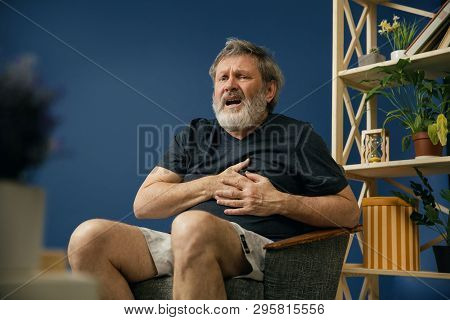 The Last Moment. Old Bearded Man In Black Shirt Sitting On The Chair And Suffering From Heart Pain O