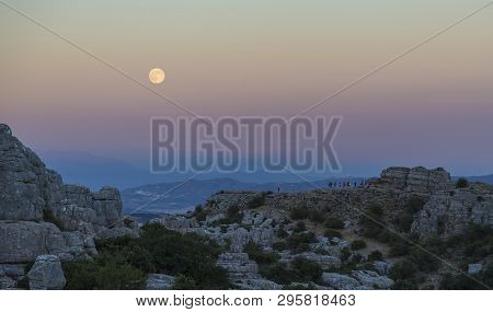 A Big Moon Rising Over The Torcal De Antequera In Spain And A Group Of People Admiring It.
