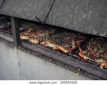 Prawns In Grilling Basket Being Grilled Streetside On​ Dusty Charcoal Stove And Turning Orange.