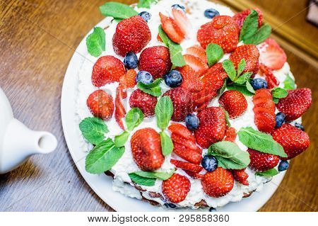 Strawberry Cake In Cream And Mint Leaves On The Table In A Plate, On The Background Of A Teapot With