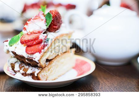A Piece Of Strawberry Cake In Cream And Mint Leaves On A Table In A Plate, In Front Of A Teapot With