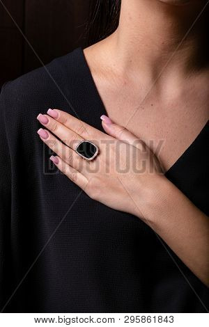 Womens Gold Ring With Black Stone In The Middle And Diamonds Fringe On Finger, On A Black Background