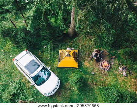 Couple Sitting Near Campfire Drinking Tea. Yellow Tent And White Suv Car. Active Leisure Time