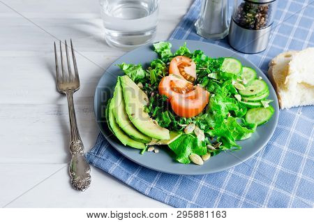 Fresh  Green Salad With Cucumber, Lettuce, Avocado And Tomatoes And Glass Water On A White Wooden Ta