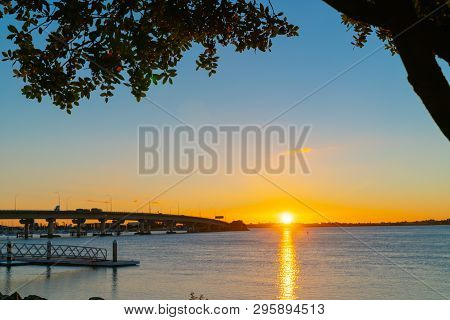 Sunrise  Glows Across Tauranga Harbor With  Curving Lines Of Harbor Bridge  And Jetty Framed By Silh