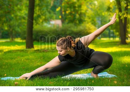Flexible Woman Plus Size In The Park On The Lawn Performs Stretching Exercises