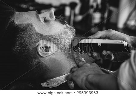 Client During Beard Shaving In Barbershop. Young Handsome Barber And Attractive Bearded Man. Black A