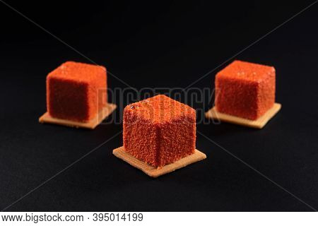 Closeup View Of Matte Fresh Dessert Isolated On Black Studio Background. Three Small Orange Square M