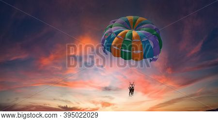 Two People Enjoy Parasailing Flight During Sunset Bright Pink And Violet Colorful Sky Background. Ex