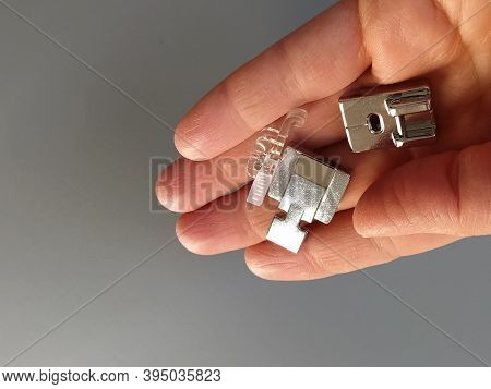 A Set Of Feet For An Electric Sewing Machine In A Female Hand. Gray Backdrop. Standard Sewing Or Zig