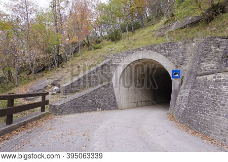 Tunnel Entrance In The Mountain With Road And Wood Guardrail