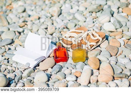 Beach Hat On Opened Book With Sunscreen And Shoes On Pebble Beach
