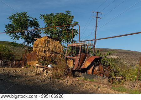 Old Rusty And Abandoned Tractor On The Street With Some Fodder In The Background In The Town Of Azok