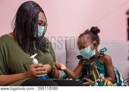 African Americans' Mother And Daughter Wearing A Mask Are Washing Their Hands With Alcohol To Protec