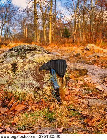 A Small Throwing Axe Leaning On A Rock In An Autumn Field