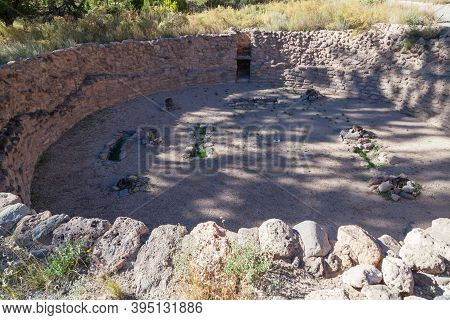 A Historical Kiva House Built Into The Ground With Shade From Nearby Trees At Bandelier National Mon