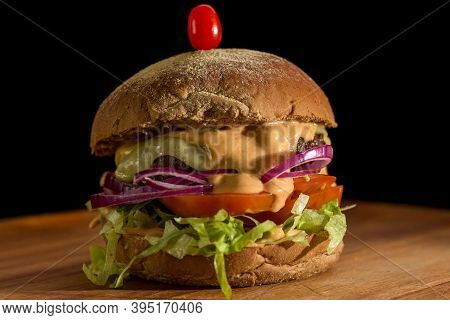 Close Up Of A Homemade Burger With Salad On A Chopping Wood Board, On Black Background. Australian B